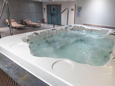 Moderner Whirlpool in einem Entspannungsbereich mit Liegestühlen im Hintergrund.