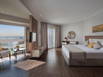 Modernes Hotelzimmer mit großem Bett, Sitzbereich und Meerblick durch bodentiefe Fenster.