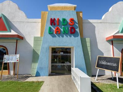 Buntes Gebäude mit der Aufschrift ‚Kids Land‘, Eingang in freiem Gelände mit Schildern.