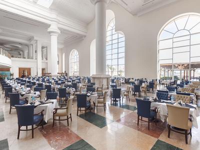Großer, heller Speisesaal mit weißen Wänden und blauen Stühlen.