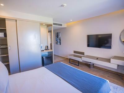 Modernes Hotelzimmer mit Bett, Fernseher, Schreibtisch und offenem Kleiderschrank.