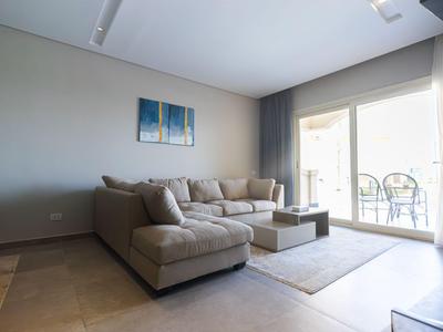 Helles Wohnzimmer mit grauem Ecksofa, Couchkissen, Teppich und Balkon mit Stühlen.