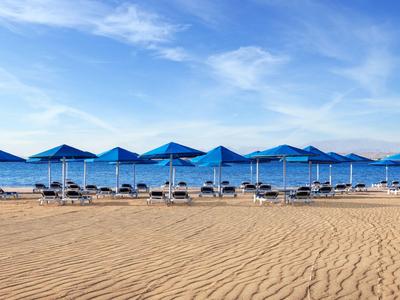 Reihe blauer Sonnenschirme und Liegestühle am Sandstrand unter blauem Himmel