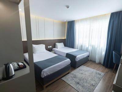 Modernes Hotelzimmer mit zwei Einzelbetten, grauem Teppich und großen Fenstern mit blauen Vorhängen.