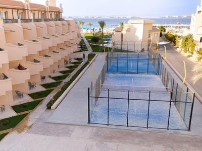 Moderner Hotelkomplex mit Terrassen und einem Platz mit Glaswänden, Meer im Hintergrund.