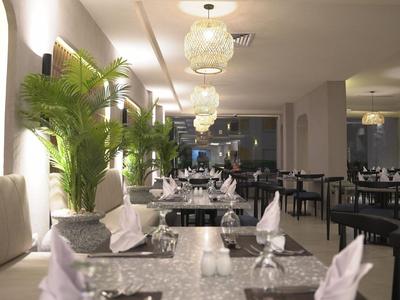 Elegantes Restaurant mit weißen Tischen, Lampen und grünen Pflanzen im Innenbereich.