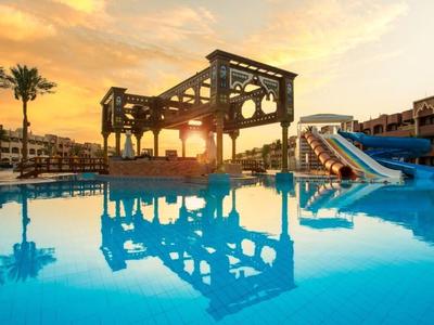 Une piscine d'hôtel avec toboggans sous un ciel coloré au coucher du soleil.