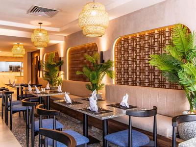Restaurant d'hôtel moderne avec tables dressées, éclairage chaleureux et plantes vertes.