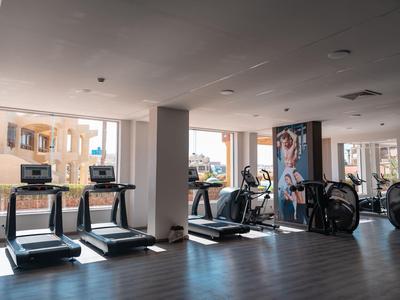 Salle de sport lumineuse avec tapis de course et vélos près de grandes fenêtres donnant sur l'extérieur.