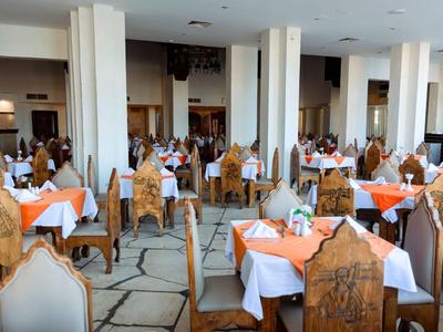 Großer Speisesaal mit vielen Tischen und geschnitzten Holzstühlen, gedeckt mit weißen und orangen Tischdecken.