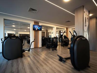 Moderner Fitnessraum mit verschiedenen Trainingsgeräten und Holzboden in einem Hotel.