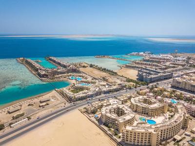 Luftaufnahme eines großen Resorts mit Pools an einem blauen Meer in einer Wüstenumgebung.