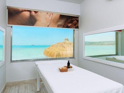 Helles Behandlungszimmer mit Meerblick, Massageliege und Spiegeln an den Wänden.