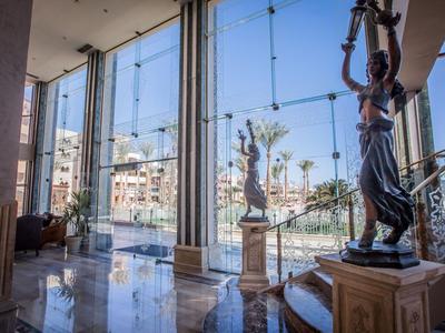 Innenansicht eines modernen Hotels mit Statuen und großen Glasfenstern mit Blick auf den Hafen.