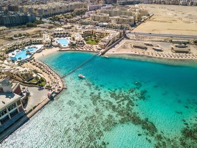Blick auf ein Resort mit Poolanlagen und klarem türkisfarbenem Wasser neben einer Sandlandschaft.