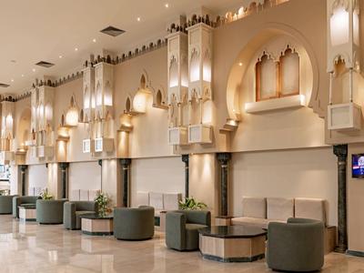 Hotel-Lobby mit hohen Wänden, dekorativen Leuchten und Sitzbereichen in neutralen Farben.