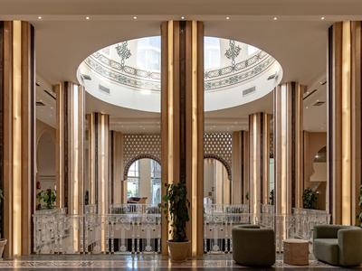 Eleganter Hotellobby mit hohen goldfarbenen Säulen, runden Möbeln und einem runden Oberlicht.