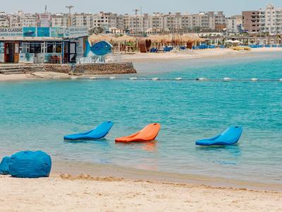 Strand mit bunten Sitzsäcken im flachen Wasser und Strandbar im Hintergrund.