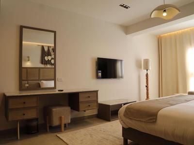 Bright hotel room with wooden furniture, bed, TV, and large curtain window.