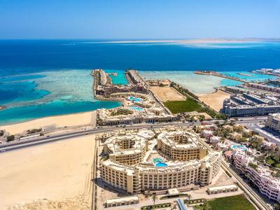 Blick auf eine Hotelanlage am Strand mit Pool und nahe am türkisfarbenen Meer.