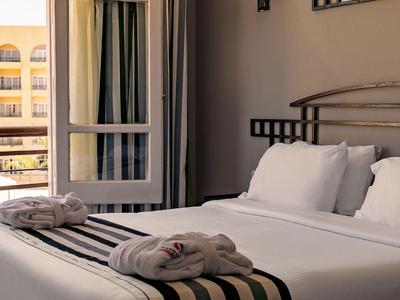 Brightly lit hotel room with bed, white pillows, and view of balcony with railing.