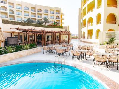 Außenbereich eines Hotels mit kleinem Pool, Tischen und Stühlen, umgeben von hellen Gebäuden.