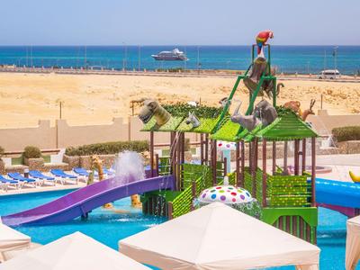 Bunter Wasserspielplatz mit Rutschen und Tierfiguren, Meer im Hintergrund.