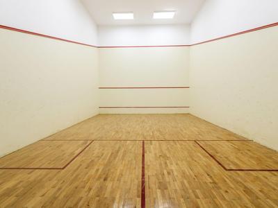 Empty squash court with wooden floor and white walls under bright lighting