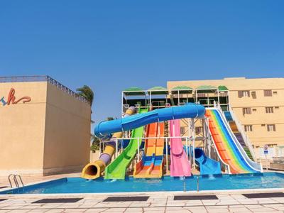Several wide, colorful water slides lead into a pool in front of a hotel building.