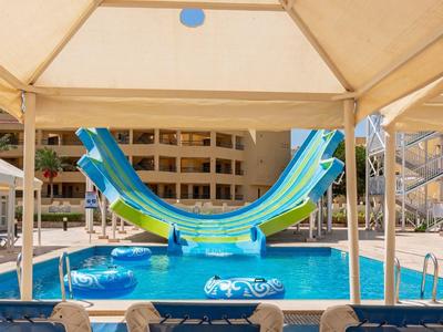 Ein Schwimmbad mit Wasserrutschen und Liegestühlen unter Sonnenschirmen in einem Hotel.