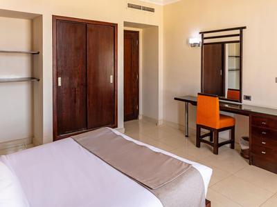 Hotelzimmer mit Bett, Schreibtisch, Stuhl und Kleiderschrank in hellen Farben.