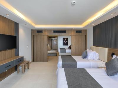 Moderní hotelový pokoj se dvěma postelemi, televizí na stěně a nepřímým stropním osvětlením.