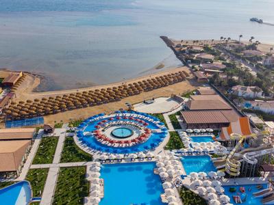 Letecký pohled na přímořské letovisko s bazény, lehátky a přístupem na písečnou pláž.