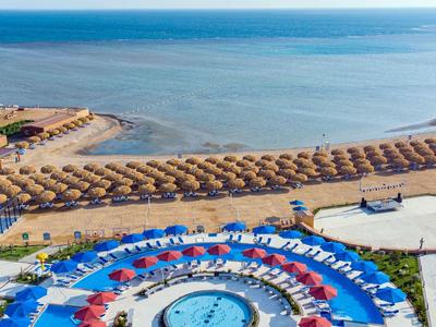 Pohled na pláž s řadami slunečníků a hotelový bazén s lehátky.