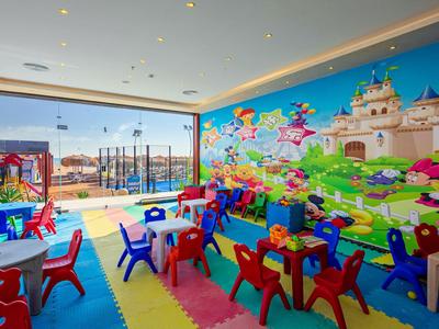 Barevná herna pro děti s malými stolky, židlemi a pohádkovou malbou na zdi.