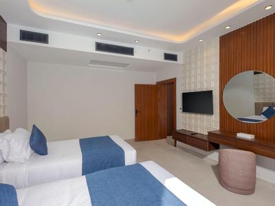 Moderní hotelový pokoj se dvěma postelemi, dřevěnými doplňky a velkým kulatým zrcadlem.