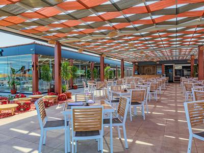 Velká zastřešená terasa s bílými židlemi a dřevěnými stoly v hotelové restauraci.