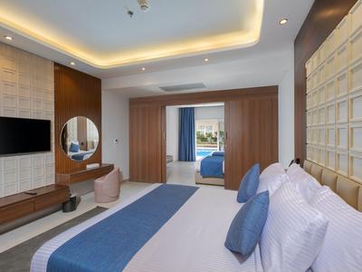 Moderní hotelový pokoj s velkou postelí, TV s plochou obrazovkou a stolem s kulatým zrcadlem.