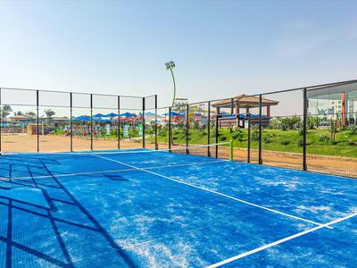 Modré hřiště na padel s plotem a slunečníky v pozadí za jasné oblohy