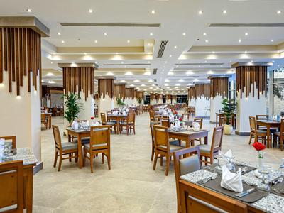 Světla hotelová restaurace s dřevěnými obklady, prostřenými stoly a moderním osvětlením.