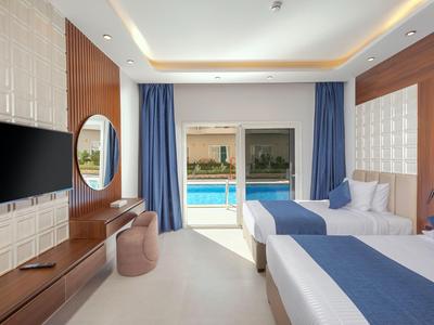 Moderní hotelový pokoj se dvěma postelemi, modro-bílým povlečením a balkonem s výhledem na bazén.