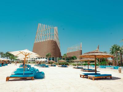 Sandstrand mit blauen Liegen und modernen, konischen Hotelgebäuden unter klarem Himmel.