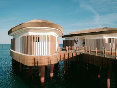 Moderne Überwasser-Bungalows mit Holzsteg und Dach über ruhigem Wasser bei klarem Himmel.