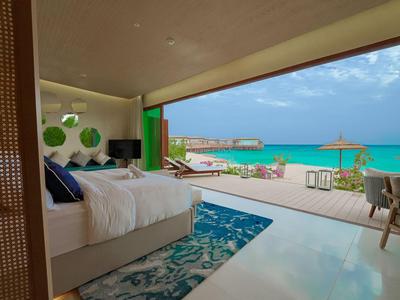 Modernes Schlafzimmer öffnet sich zu einer Terrasse mit Blick auf türkisfarbenes Meer und Sandstrand.