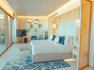 Helles Hotelzimmer mit großem Bett, Sofa, TV und Zugang zu einer Terrasse.
