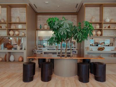 Moderner Hotel-Loungebereich mit Holztischen, schwarzen Hockern und großen grünen Pflanzen.