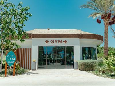 Hotelgymnasium mit modernem Eingang, umgeben von Palmen und Grünflächen unter klarem Himmel.