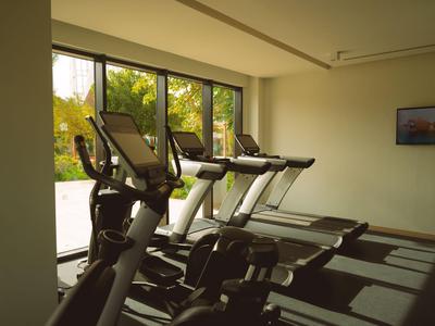 Innenraum mit Laufbändern vor großen Fenstern und Blick auf Bäume im Fitnessbereich eines Hotels.
