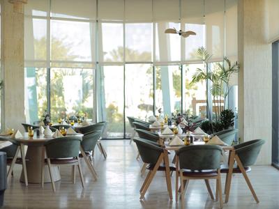 Helles Hotelrestaurant mit großen Fenstern, grünen Stühlen und gedeckten Tischen.