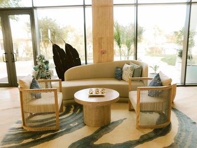 Helles Wohnzimmer mit Sofa, zwei Stühlen und rundem Tisch auf einem gemusterten Teppich in Hotel-Lounge.